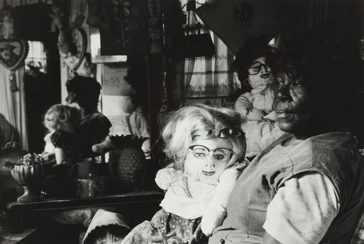 Nellie Mae Rowe sits in a darkened room with a doll on her lap.